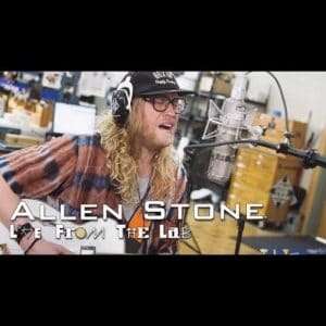 Allen Stone singing into a microphone with headphones and a cap in a video still from Live From The Lair